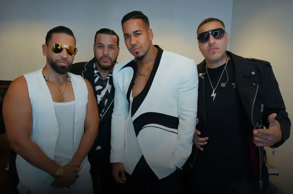 Aventura, Four men stand together for a group photo against a plain background. All are dressed stylishly: three wear black and white outfits, with one in a white blazer with black trim, and the fourth wears an all-black outfit with sunglasses and a lightning bolt necklace, reminiscing on their Aventura Madison Square Garden concert.