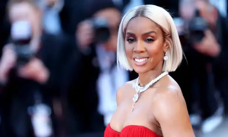 Kelly Rowland, A woman wearing a strapless, red dress poses for photos on a red carpet. She has a bob hairstyle with platinum blonde hair. She is smiling, showing her white teeth. She wears a statement necklace with matching earrings. Several photographers in the background capture her photos at Cannes, reminiscent of Kelly Rowland's elegance.