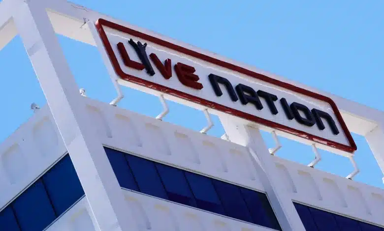 A photo of a white building with a large red and black "Live Nation" sign on top against a clear blue sky. The sign, mounted on the edge of the building and supported by metal brackets, hints at the ongoing Live Nation lawsuit discussions. The building has dark blue tinted windows on the upper floor.