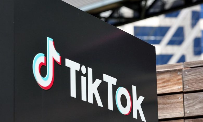 A close-up view of a prominent tiktok logo on a black background, displayed on a signage board, with parts of architectural structures partially visible in the blurred background.