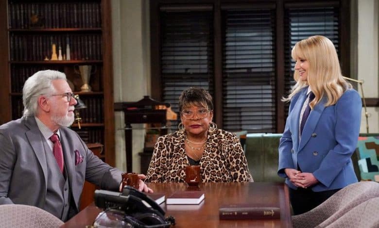 Three people in a professional office setting. a man in a suit and a woman in a blue blazer listen attentively to a woman in a leopard print top and glasses, who is speaking and gesturing with her hand.