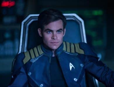 A man in a starfleet uniform sits thoughtfully in a dimly lit spaceship cockpit, his expression serious, focused on something beyond the view of the camera.