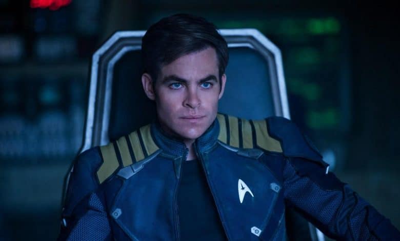 A man in a starfleet uniform sits thoughtfully in a dimly lit spaceship cockpit, his expression serious, focused on something beyond the view of the camera.