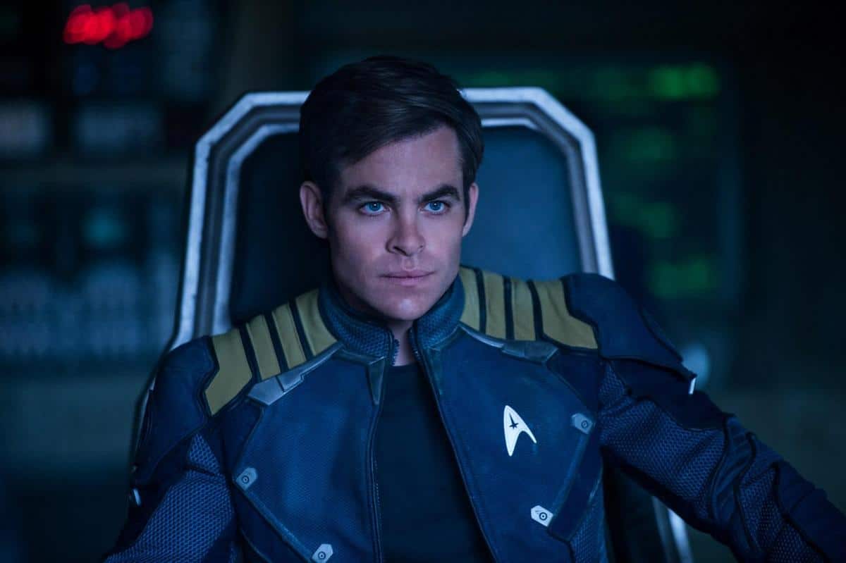 A man in a starfleet uniform sits thoughtfully in a dimly lit spaceship cockpit, his expression serious, focused on something beyond the view of the camera.