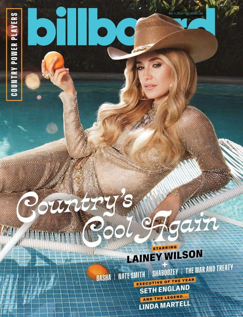 A woman in a sparkling, gold dress and cowboy hat lounges on a white pool float, holding an orange. She has long blonde hair and poses by the water. The "billboard" magazine cover headline reads "Country’s Cool Again," highlighting Lainey Wilson and other artists.