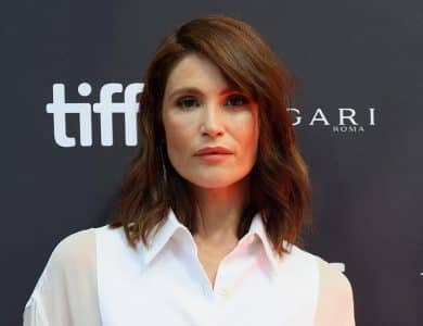 A woman with shoulder-length brown hair poses at the toronto international film festival, wearing a simple white blouse. the background features the festival's logo and the sponsorship logos for bulgari and roma.