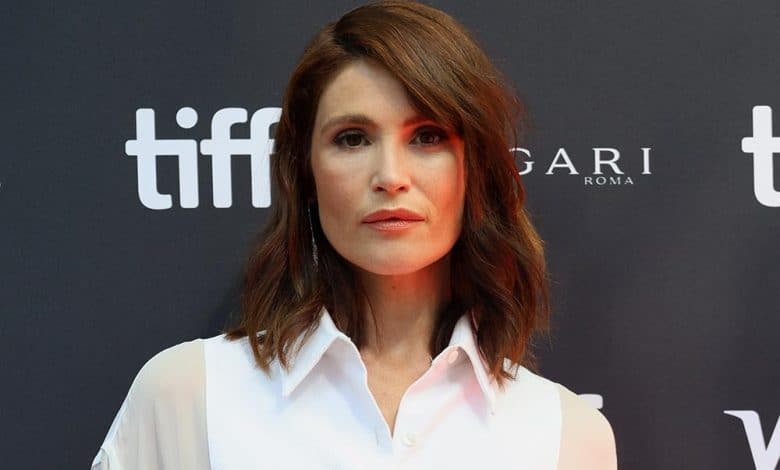 A woman with shoulder-length brown hair poses at the toronto international film festival, wearing a simple white blouse. the background features the festival's logo and the sponsorship logos for bulgari and roma.