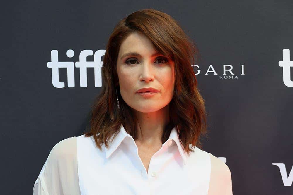 A woman with shoulder-length brown hair poses at the toronto international film festival, wearing a simple white blouse. the background features the festival's logo and the sponsorship logos for bulgari and roma.