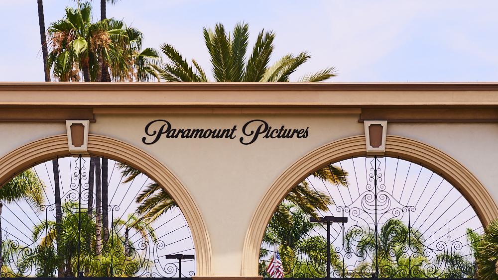A close-up view of the top arches of the paramount pictures entrance gate, featuring elegant wrought-iron details and lush palm trees visible in the background under a clear sky.
