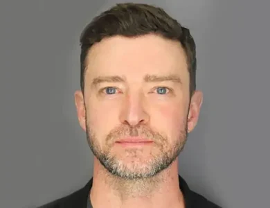 Justin Timberlake, A man with short, dark hair and a trimmed beard is looking directly at the camera with a neutral expression. He is wearing a dark shirt, and the background is plain and gray, focusing attention on his facial features.