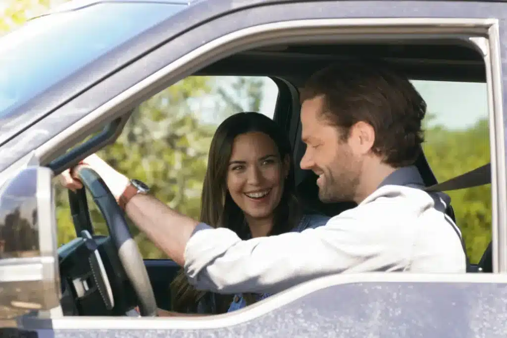 Odette Annable as Geri Broussard, Jared Padalecki as Cordell Walker, A man and a woman are sitting in the front seats of a vehicle. The man, seated in the driver's seat, is smiling and steering, while the woman seated next to him is looking at him and smiling. They appear to be engaged in a pleasant conversation. Trees and greenery are visible through the windows.