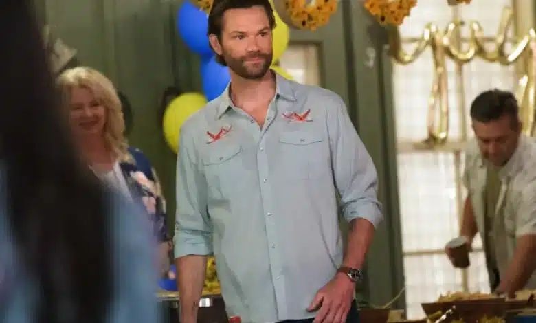 Jared Padalecki, A man with short brown hair and a beard, wearing a light blue shirt with embroidered patterns, stands indoors at a gathering. Behind him are festive decorations, including sunflower garlands and yellow and blue balloons. Two people in casual attire are visible in the background.