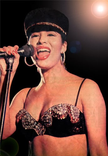 Selena Quintanilla, A woman with dark hair is singing into a microphone under bright stage lights. She wears a sequined black hat, large hoop earrings, and a shimmering black and gold bralette. The background is dark, with a lens flare effect near the top right corner, creating a dramatic atmosphere perfect for celebrating Hispanic Heritage Month.