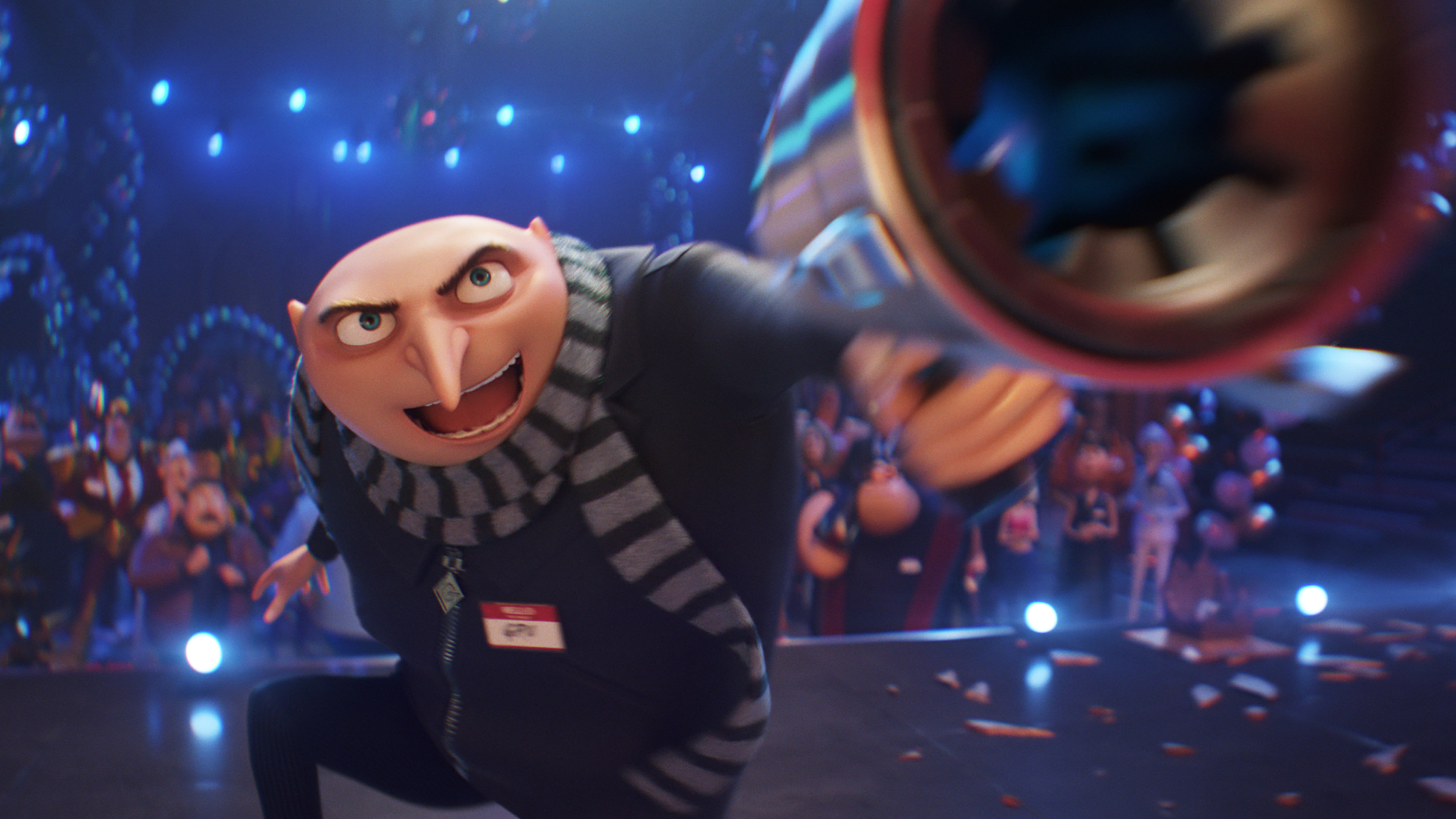 An animated character with a bald head and a distinctive long nose wears a black coat and striped scarf. He points a large blaster weapon, creating a motion blur effect. In the background, colorful lights and various characters suggest the dynamic scene of a Universal Pictures family movie.