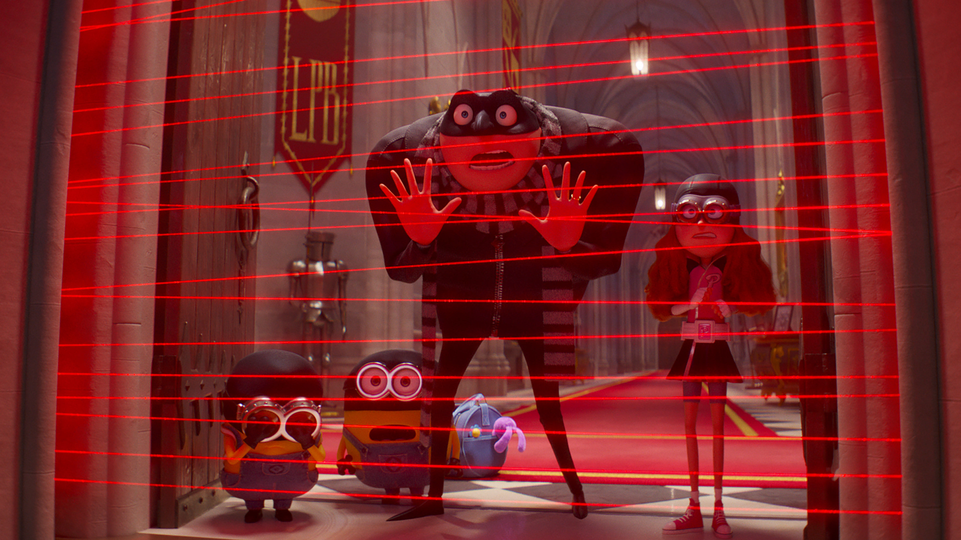 A group of animated characters stands in a hallway with red laser beams forming a security grid. A tall character in black holds his hands up cautiously. Two small yellow characters from *Despicable Me 4* look distressed while another peers through goggles. This scene brings the excitement Universal Pictures is known for, reminiscent of Steve Carell's iconic style.
