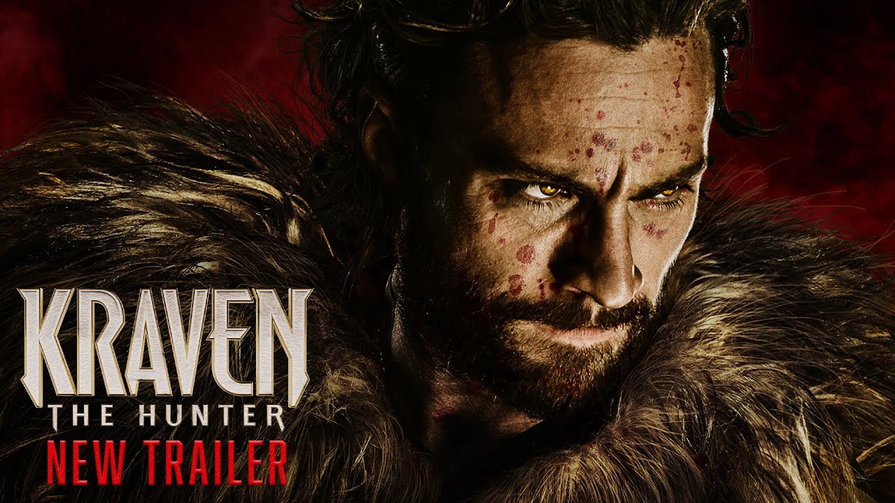 Kraven The Hunter, A man with a rugged beard and intense expression wears a fur-lined outfit, his face marked with dirt and scratches. The background is a dark red. Text on the left reads "Kraven The Hunter" in white, stylized font, with "New Trailer" in red below it.