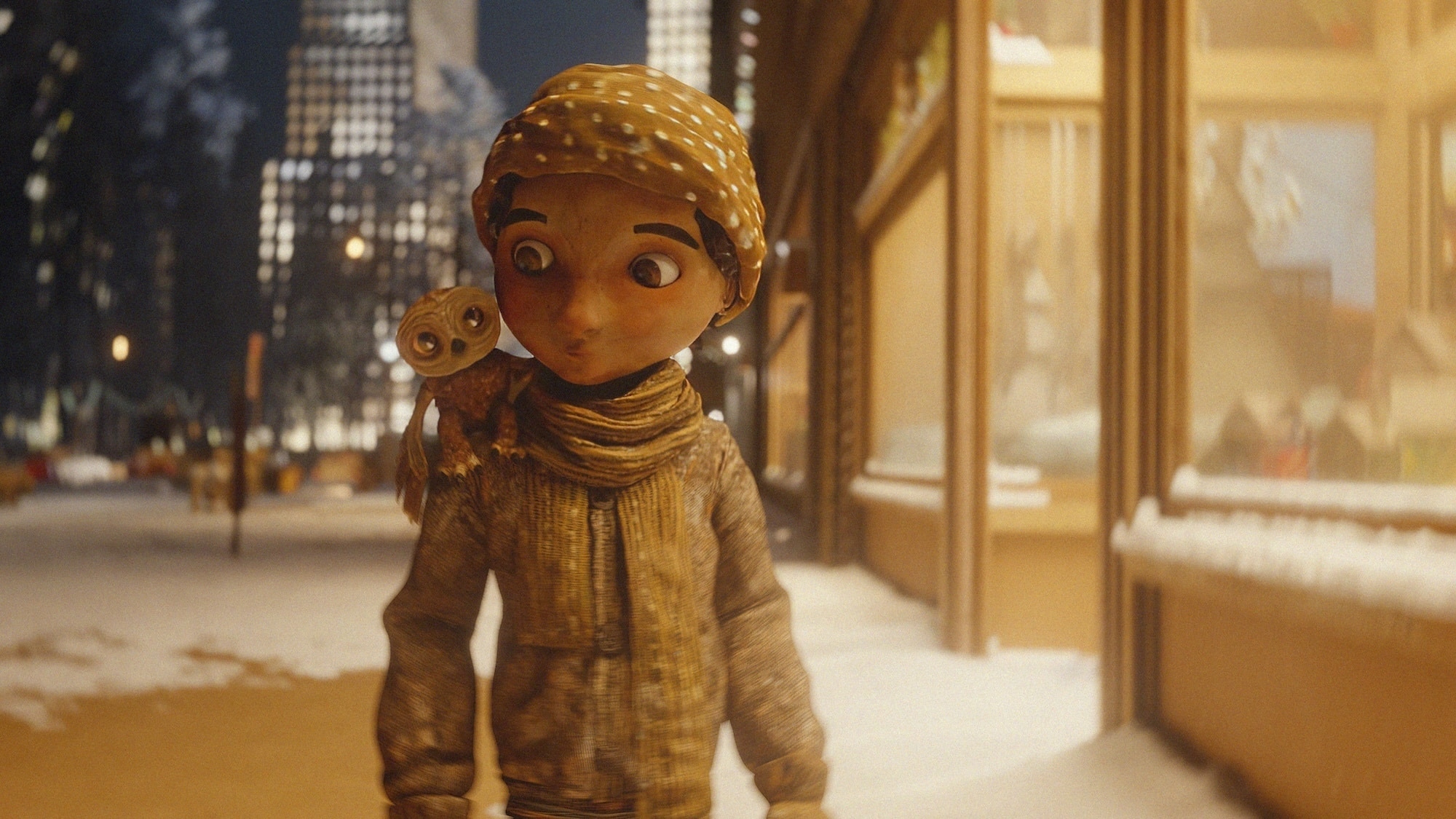 A 3D-animated character with a large hat and scarf walks in a snowy city at night, with brightly lit buildings behind. The character has a small bird perched on their right shoulder. The scene is warmly lit by the glow of streetlights and shop windows, with snow on the ground and ledges.