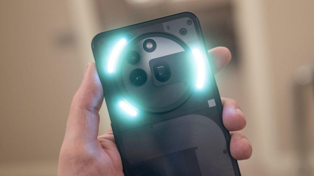 A hand holds a modern smartphone upside down, showing its back. The phone features a circular camera module with three lenses and two bright, curved LED light strips illuminated around the circle. The background is blurred and neutral.