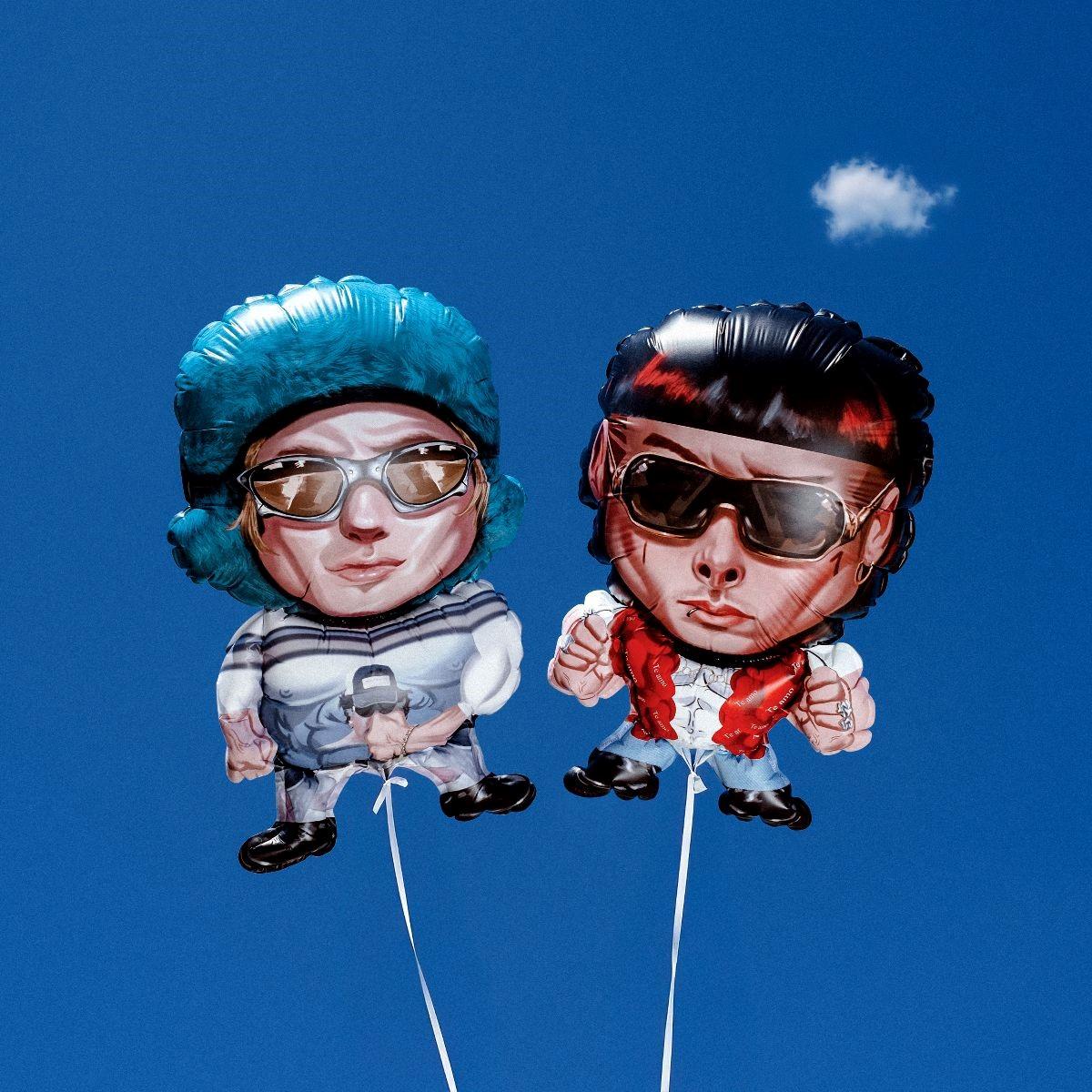 Two cartoon-style balloons float against a clear blue sky with a small white cloud. The left balloon shows a person with blue hair, sunglasses, and a blue outfit. The right balloon depicts a person with black hair, red scarf, and sunglasses. Both have exaggerated features.